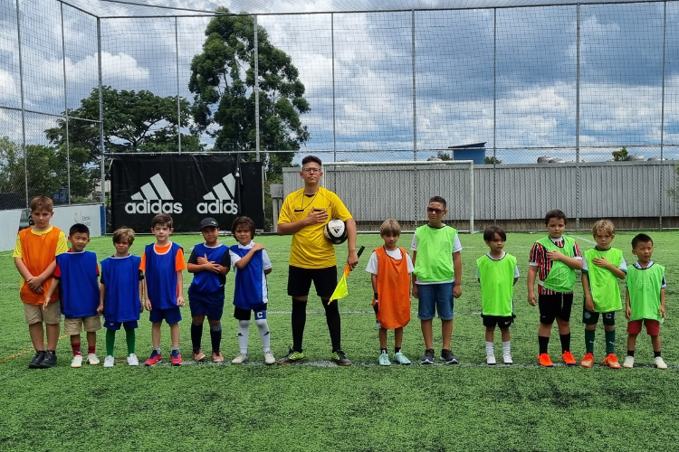 Crianças uniformizadas em torneio de futebol com árbitro
